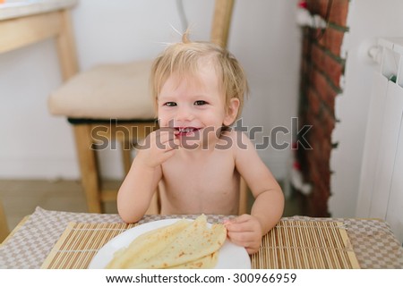 Cute baby eating a pancake sitting by a small wooden table