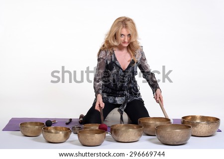 Woman playing tibetan singing bowl in photo studio on white background.