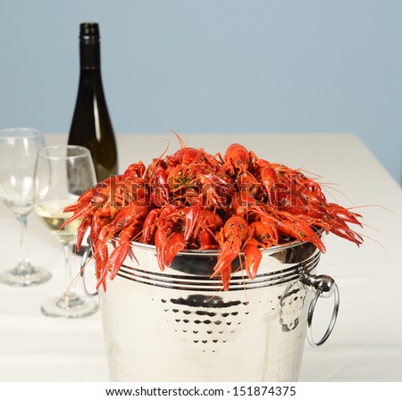 silver pail full of river lobster with wine and glasses on white table linen.