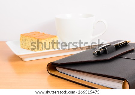 black organizer with black pen coffee and cake ,coffee break on wooden table