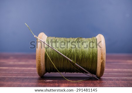Vintage grunge wooden green thread spool with needle on wooden board background