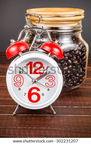 Coffee time,alarm clock with white coffee cup and coffee bean in glass bottle on wooden background