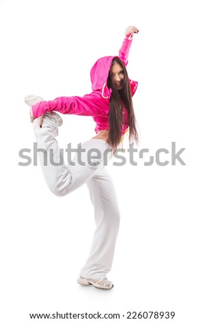 Young modern flexible hip-hop dance girl standing on one leg. Female in white sweatpants and a pink hoodie and sneakers standing on isolated white background.
