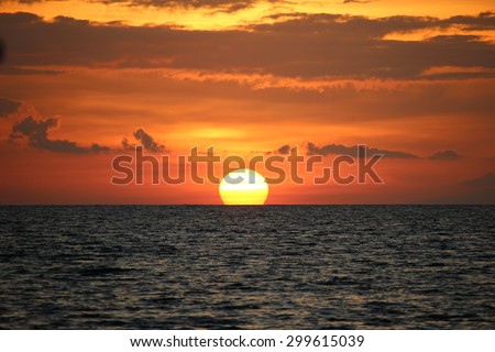 Sun sets into the sea. Sun sinks into the ocean. Golden sky. Grey sea. Tropical sunset. Bali sunset. Sun touching the horizon.