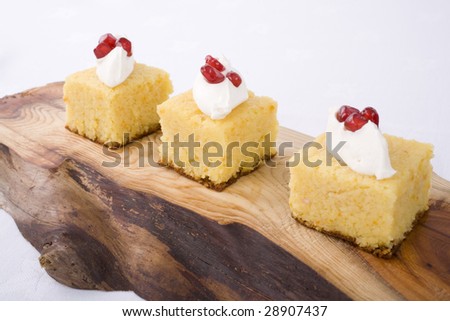 Orange and almond cake with cream and pomegranate seeds, served on wooden platter.