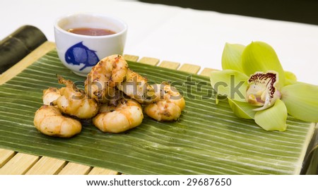 Jumbo prawns with Thai sweet chili dipping sauce on a banana leaf, with an orchid for garnish.