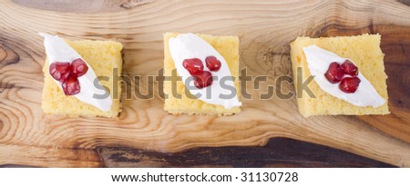 Orange and almond cake with cream and pomegranate seeds, served on wooden platter.
