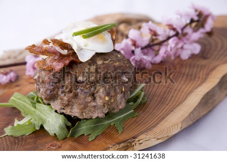 Gourmet Burger on rocket bed, with bacon and quail\'s egg on top and served on wooden platter with wild flowers.