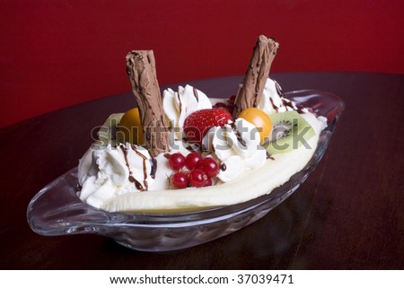 Banana Split with kiwi fruit, strawberry, redcurrants, physalis, chocolate flakes, cream and chocolate sauce in a glass dish.