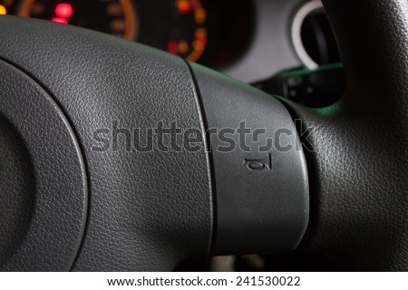Close up of a steering wheel with a horn symbol showing on the horn pad. Partial dashboard lit display in the background.