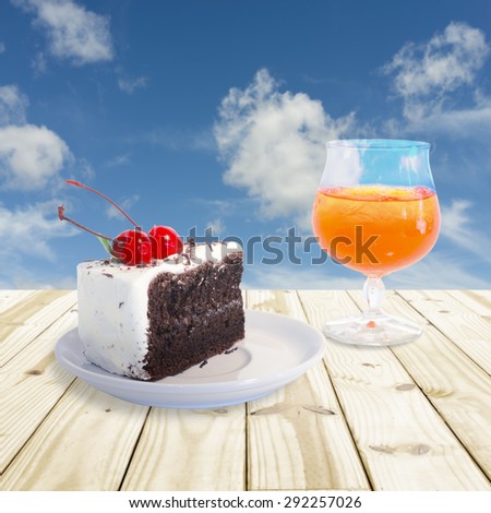 Cherry chocolate cake and Orange juice setting on wood table.  Blue sky blurry background.  Soft focus on cherry