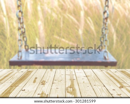 Wood table top on old wood swing in meadow blurred background