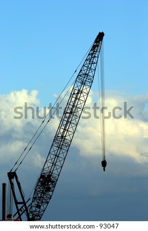 A large crane is silhouetted against a bright blue sky with clouds rolling in.