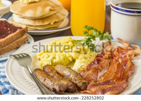 large hot breakfast with scrambled eggs and bacon sausage served with pancakes and toast \