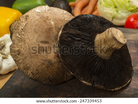 Portobello mushrooms on a cutting board with fresh salad ingredient in the background\