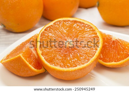 fresh cut orange on a plate with whole oranges in background on a white tablecloth\