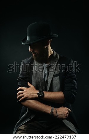 The brutal bearded man in a black bowler hat rolls up sleeves of his jacket