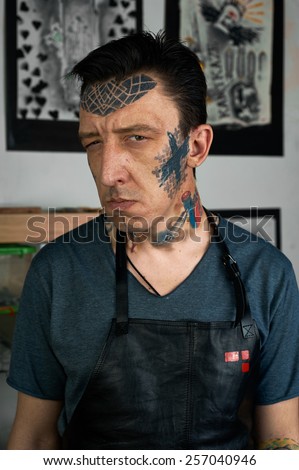 Tattooed man in black leather apron making faces
