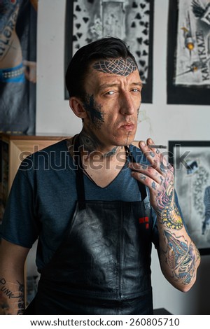 Tattooed man in leather apron smoking a cigarette