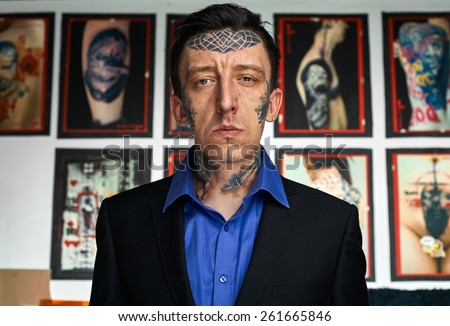 Man with tattooes on face in black jacket and blue shirt
