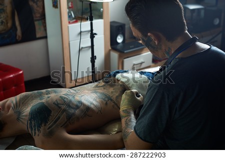 Tattoo master working in studio. View from back