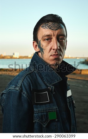 Fashion Portrait of handsome Guy with tattooed Face in denim Jacket on Street