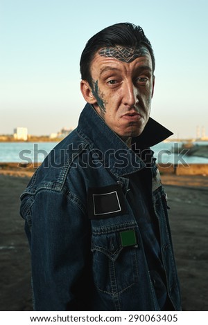 Hooligan with tattooed Face in denim Jacket on Street making Faces