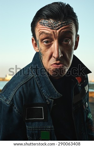 Man with tattooed Face in denim Jacket on Street making Faces