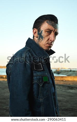 Fashion Portrait of serious Man with tattooed Face in denim Jacket on Street