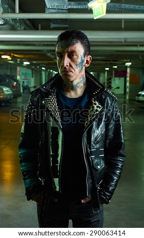 Portrait of Man with tattooed Face in leather Jacket on Parking