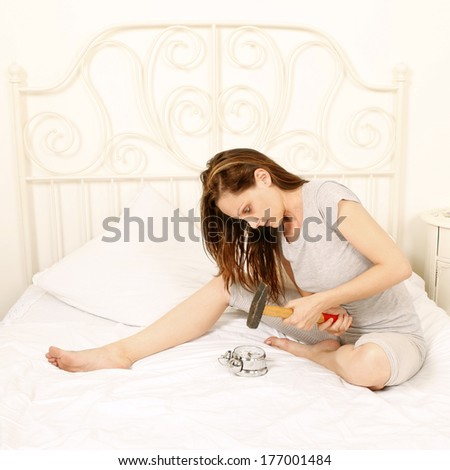 Angry woman smashing alarm clock with hammer