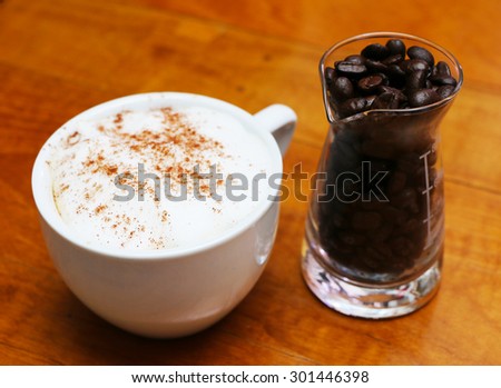 Coffee beans in a glass measuring cup and coffee cup on the table.
