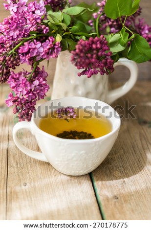 Herbal tea in a glass cup, a metal strainer with dry flowers marjoram, fresh flowers of oregano on the background of wooden boards