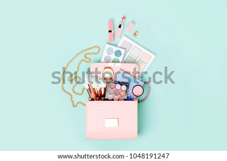 Cosmetic products flowing from Makeup bag on pastel blue background.  Flat lay, top view. Fashion concept