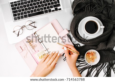 Woman writes in the planner. Workspace with laptop,  coffee cup wrapped in scarf, golden clips, glasses. Stylish office desk. Autumn or Winter concept.  Flat lay, top view
