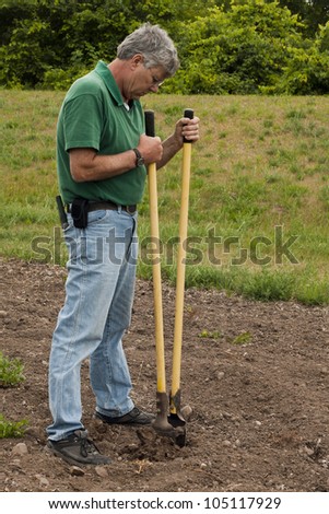 man preparing to erect a fence by digging a post hole