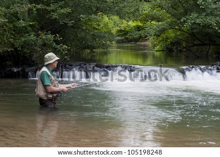 man fishing for trout next to a small waterfall
