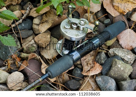 vintage casting reel and rod lying on a stream bank