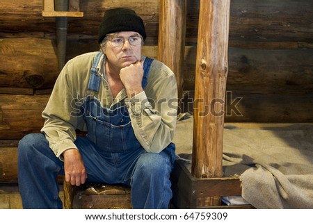 man in bib overalls sitting in his log cabin thinking about life