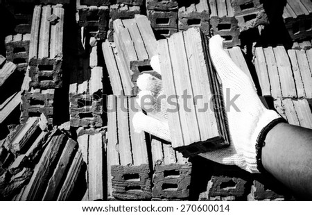 Safety a hand by white glove for working time of labor,workman with many brick ready for construction.Focus on a white glove and brick in a hand also with black and white color