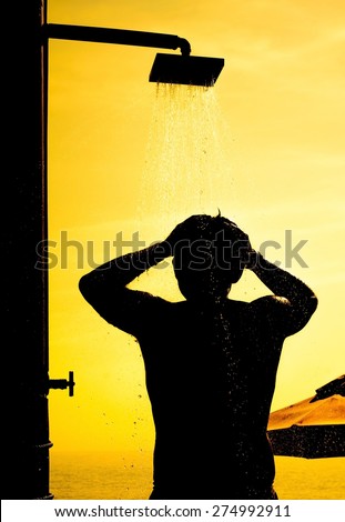 Silhouette of a man took a shower  after playing on the beach with sunset time,Focus on a man and blurry on drop of water