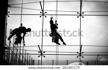 Dangerous working of a man on high Tower in the city with skycraper windows cleaner on black and white color
