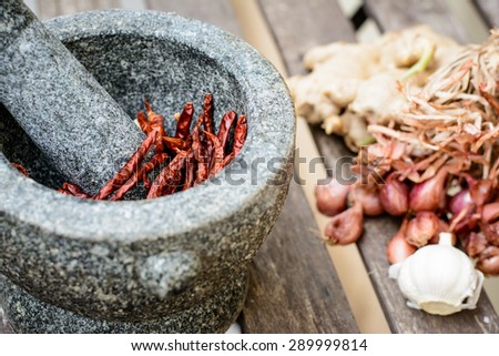 Stone mortar in thai kitchen style put on the wooden table,Focus on red chili in a mortar