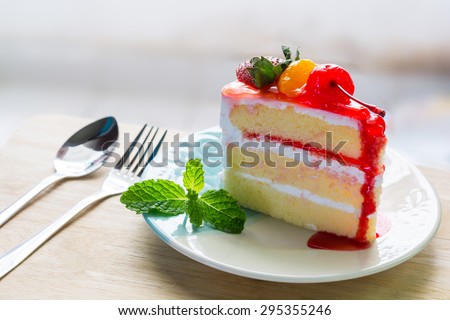 Fruit cake delicious, vanilla cake topping with fruit decorated with whipped cream and cherries with mint on dish on wood background.