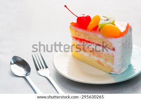 Fruit cake delicious, vanilla cake topping with fruit decorated with whipped cream and cherries with mint on dish on wood background.