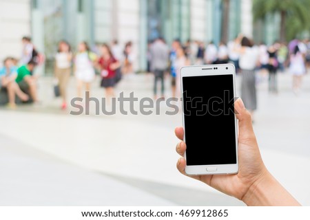 women hand holding white mobile smart phone with black blank screen with blur shopping mall or shop background