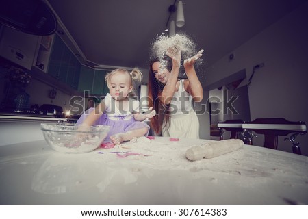young beautiful mother teaches daughter prepare dough in the kitchen