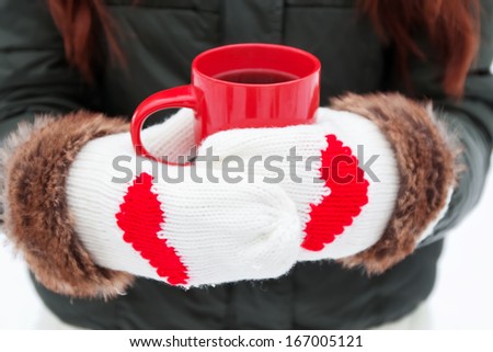 Hands in warm mittens with hearts holding red cup close-up