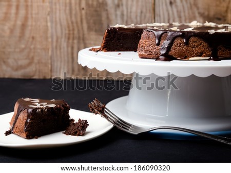 A piece of chocolate almond cake on the plate and cake on the stand