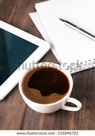 Coffee cup, tablet, paper notebook and pen on the wooden table close-up